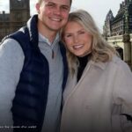Katie Bates and Travis Clark smiling together in London with the Houses of Parliament behind them